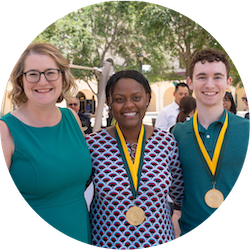 Three people smiling and posing, two of them are wearing medals