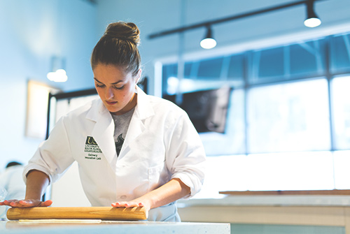 USF culinary student rolling out dough.