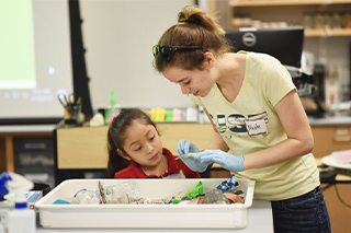 USFSM biology student Nicole Bill, right, assists a girl from UnidosNow.